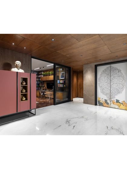 This view of the Camellias lobby looks towards the study, framed by a doorway. A pink cabinet and a whimsical door with artwork by Gond artists add a playful touch to the sophisticated material palette.