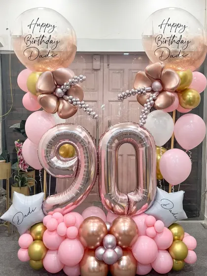 Honoring 90 incredible years with this elegant rose gold and pink arrangement. The large '90' foil balloons are complemented by delicate balloon flowers and personalized star balloons, creating a beautiful tribute for a cherished family member.
