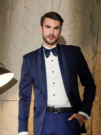 A confident, full-length portrait in the navy textured tuxedo. The classic combination with a white pintuck shirt and bow tie makes for a timeless and elegant formal look.
