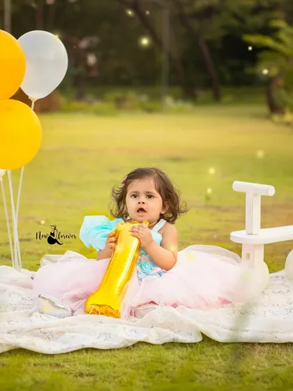 A sweet moment from an outdoor first birthday picnic. The balloons and "ONE" banner mark the special occasion in a beautiful, natural setting.