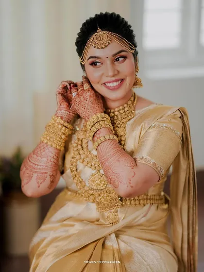 A beautiful portrait of the bride adjusting her earring, her smile radiant and her gold jewelry stunning.
