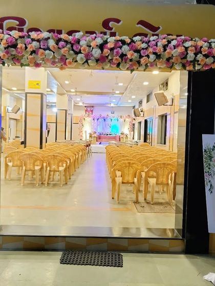 A simple yet elegant entrance for a wedding hall. The arch is decorated with dense clusters of pink, peach, and white roses, perfectly complementing the welcome sign for the couple.