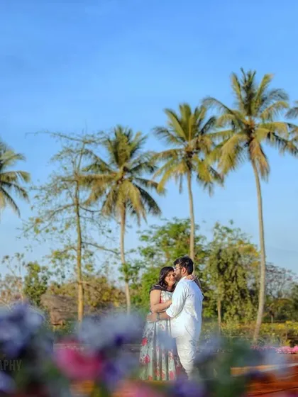 An intimate embrace framed by flowers, with the lake and palm trees in the background, creating a layered and beautiful pre-wedding portrait.