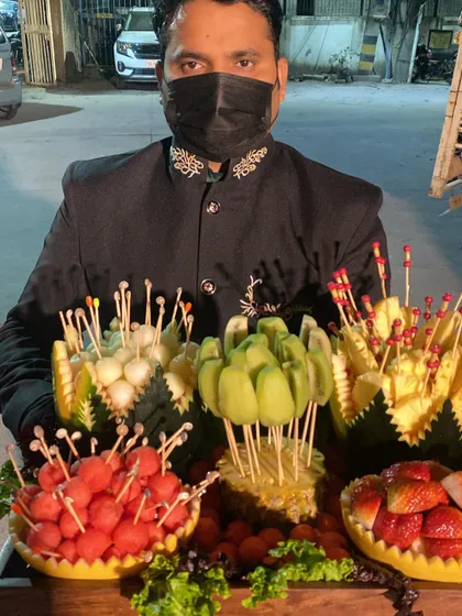 Our staff presenting an elaborate fresh fruit platter. The fruits, including watermelon, muskmelon, kiwi, and pineapple, are intricately carved and arranged on skewers for easy and elegant snacking.