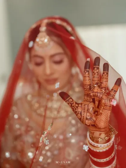 A powerful close-up of a Punjabi bride's hand, showcasing her beautiful red 'chura' and intricate mehendi. The focus on her hand, with the ring and veil, symbolizes the promises and traditions of her wedding day.