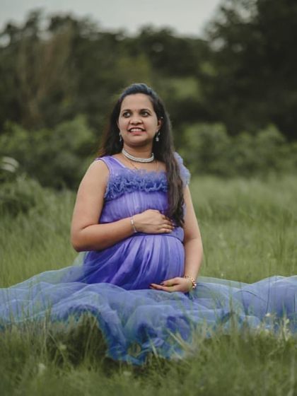 A peaceful moment in a field of green. This lavender-blue maternity gown with a ruffled neckline is perfect for a serene and natural photoshoot.