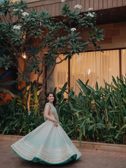 A classic bridal twirl, capturing the movement and elegance of the bride's lehenga against a backdrop of lush greenery.