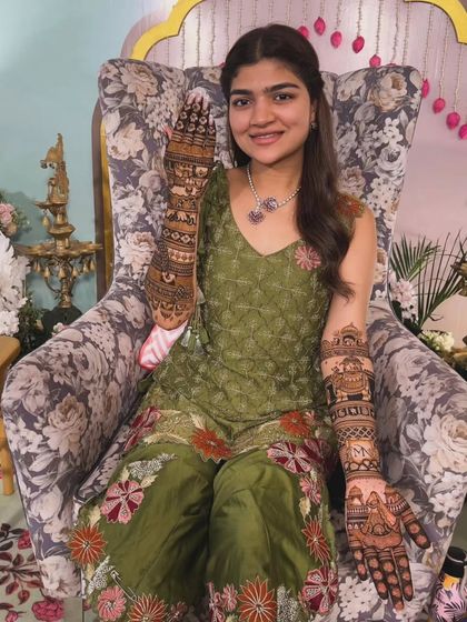 A happy bride showing off both her hands, covered in our beautiful and detailed bridal mehandi.