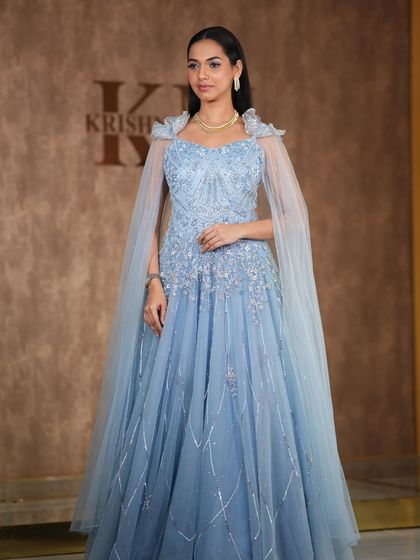 A fairytale moment in this powder blue gown with a sheer cape. The simple diamond necklace adds a touch of elegance, making it perfect for a reception or pre-wedding photoshoot.