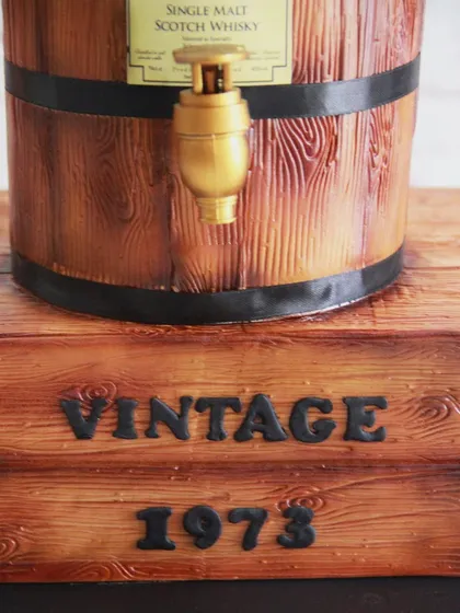 The base of the barrel cake was designed to look like a rustic wooden crate, complete with a "Vintage 1973" inscription.