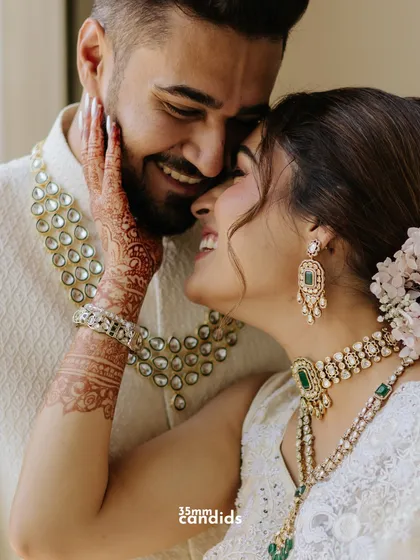 A close-up of pure joy and affection. The bride's henna-adorned hand gently touches the groom's face as they share a happy, intimate moment.