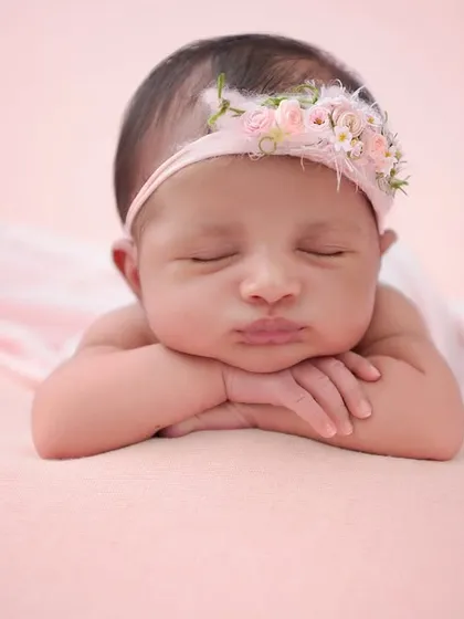 This classic newborn portrait focuses on the baby's serene expression and perfect "chin on hands" pose, highlighting their delicate features against a simple, soft pink backdrop.