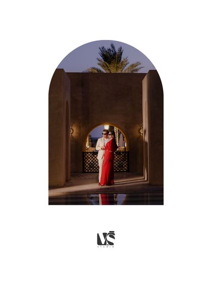 A dramatic and romantic portrait of a couple embracing under an archway at dusk in Dubai. The lighting and their reflection in the water create a cinematic and intimate atmosphere.