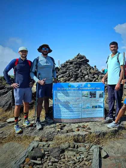 Trekkers at the Pushpagiri (Kumaraparvatha) peak, standing by the official board that marks the summit.