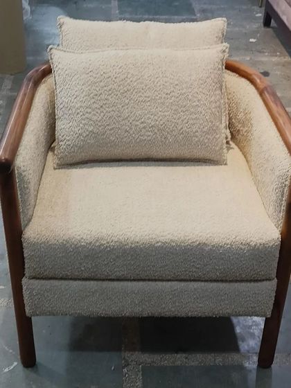 A minimalist armchair with a solid wood frame and a comfortable, textured cream-colored cushion. This piece combines natural materials with a simple design for a timeless look.