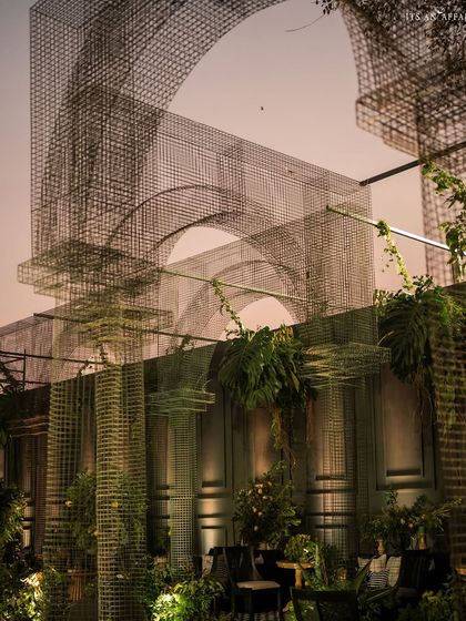 The interplay of light and shadow on the mesh arches and dark walls creates a moody and sophisticated atmosphere as evening sets in.