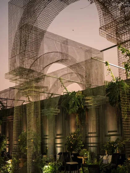 The interplay of light and shadow on the mesh arches and dark walls creates a moody and sophisticated atmosphere as evening sets in.