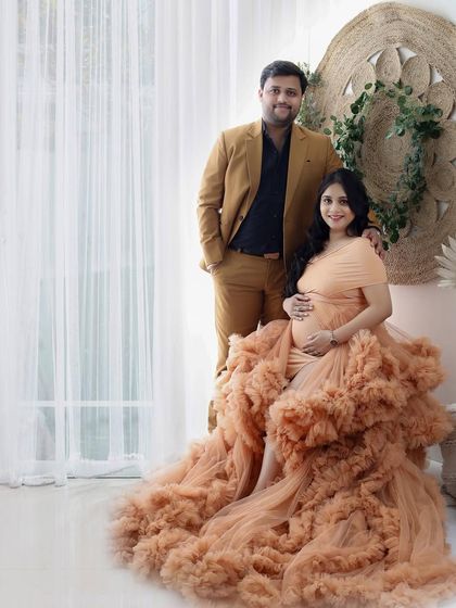 A stylish couple posing in our bright, window-lit studio. The mom-to-be's voluminous peach gown adds a touch of glamour to the earthy, boho-inspired setting.