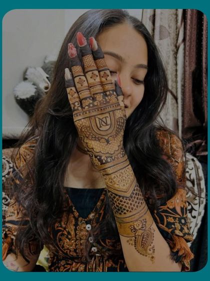 A happy client showing off her personalized mehndi, which includes her initial 'N' in a stylish monogram on the back of her hand.