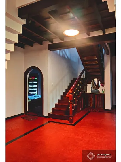 The vibrant red oxide flooring of the entrance hall leads to a beautifully crafted wooden staircase. The contrast with the white lime-washed walls is a hallmark of this style.