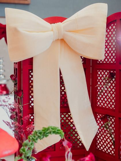 A large, elegant white bow serves as a simple yet impactful piece of decor against a red screen.