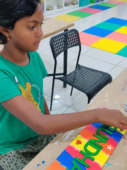 A young girl working on her vibrant, rainbow-colored nameplate during a drop-in art session.
