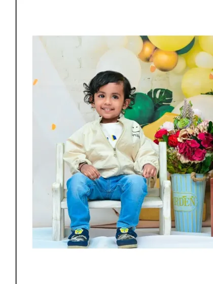 A sweet portrait of a two-year-old boy, dressed in casual jeans and a jacket, sitting comfortably for his birthday photoshoot. The soft lighting and simple props keep the focus on his happy expression.