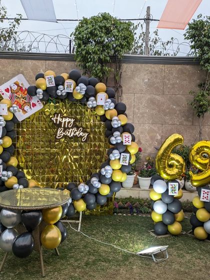 A fun casino-themed 69th birthday setup in a garden, featuring a balloon arch with playing card props and large foil numbers.
