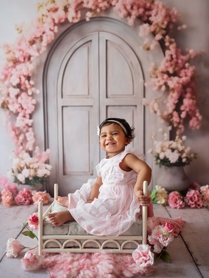 What a happy smile! This little girl is enjoying her sitter session in a lovely floral setup with a miniature bed prop.