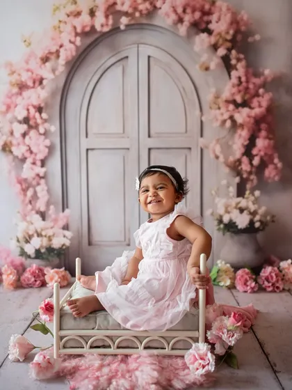 What a happy smile! This little girl is enjoying her sitter session in a lovely floral setup with a miniature bed prop.