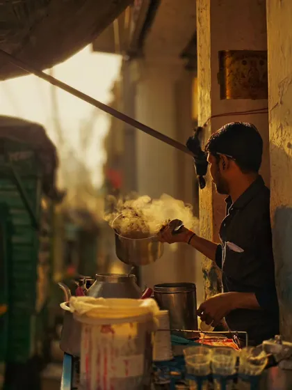 A candid shot of a chaiwala at work during the golden hour. The warm light and rising steam create a cinematic and authentic slice of life from the streets of Delhi.