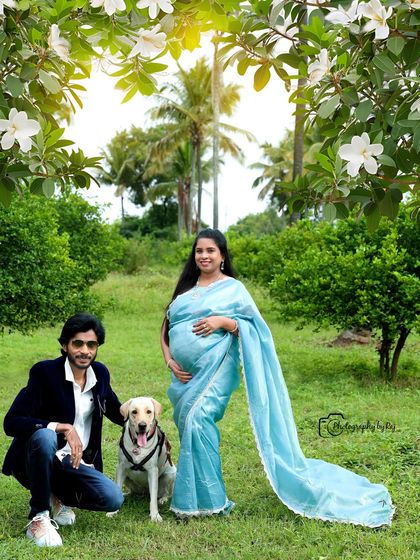 A beautiful outdoor portrait of a couple with their pet dog. The mother-to-be is wearing a lovely light blue saree.