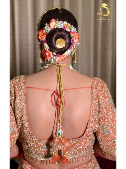 A close-up of a neat, round bridal bun decorated with a vibrant floral arrangement and a central gold accessory.