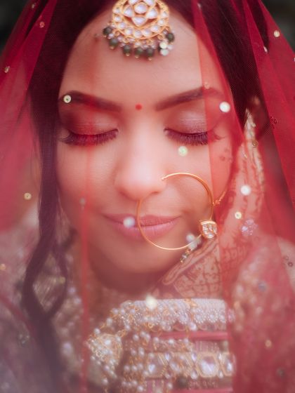 A close-up, dreamy portrait of a bride through her red veil, her eyes closed in a moment of peace.