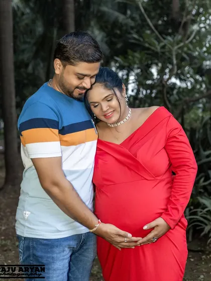 This is a close, tender moment captured outdoors amidst lush greenery. The focus is on the quiet connection and embrace, showing the love that surrounds the baby bump.