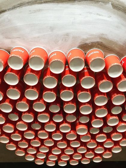 As a tribute to coffee farmers, this portrait was created live at the World Coffee Conference using waste from the Nescafé stall. The face is formed from used paper cups, and the background is a mosaic of empty coffee sachets contributed by visitors, making it a truly collaborative and sustainable piece.