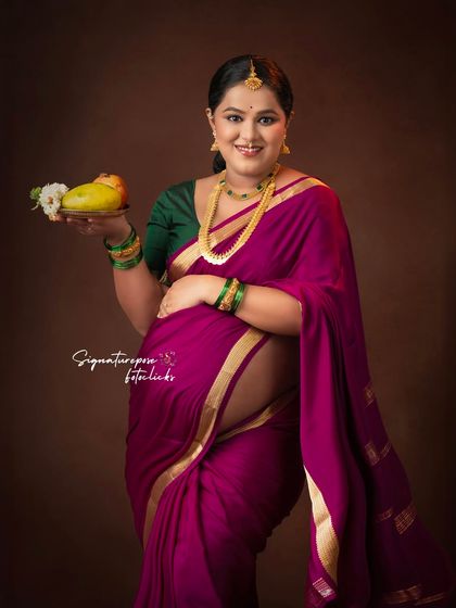 A graceful maternity portrait celebrating tradition. The expectant mother is dressed in a beautiful saree, holding a mango, which is symbolic of fertility and blessings in many Indian cultures. This is a popular style for baby shower photoshoots.