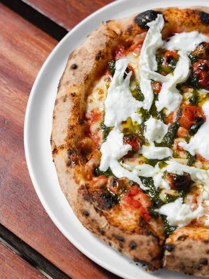 A top-down view of the Stracciatella Pizza, showcasing the generous amount of fresh cheese and pesto drizzled over the top.