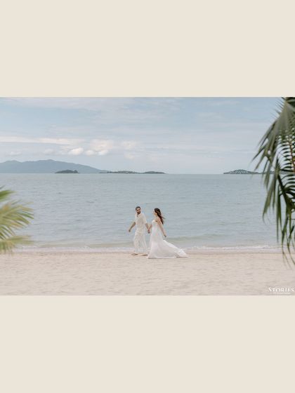 A wide, cinematic shot of the couple walking on a vast, empty beach.