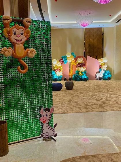 A glimpse of the party space from behind a green sequin wall, featuring a hanging monkey prop and other animal cutouts.