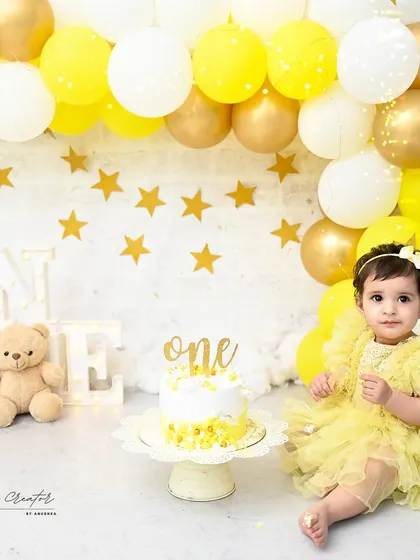 A sunny and cheerful first birthday celebration. This setup features a bright yellow balloon arch, a sweet teddy bear, and a delicious cake, creating a perfect scene for a happy one-year-old girl.