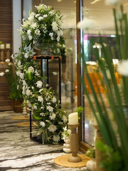 Cascading white florals on a modern black stand create a dramatic yet elegant statement piece for an event entrance, complemented by wooden candle holders for a touch of warmth.
