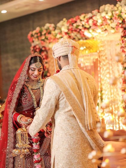 The bride and groom during the Kalire ceremony. This shot captures a traditional moment with the bride gently shaking her Kalire over her bridesmaids, framed by a beautiful floral arch.