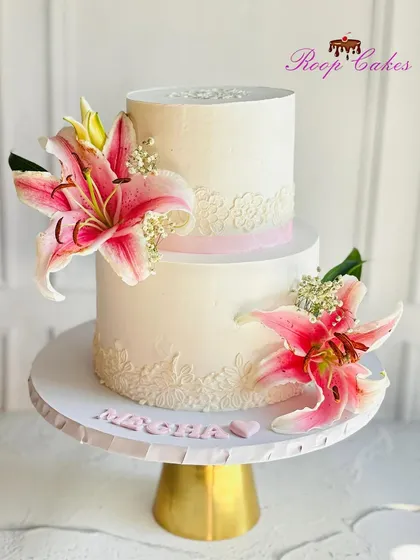 Isn't it gorgeous? This stunning two-tier cake combines a delicate lace stencil with the vibrant beauty of fresh pink lilies.