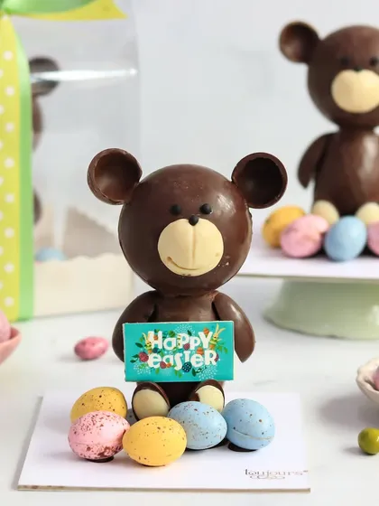 My adorable chocolate teddy bear holding a "Happy Easter" sign, surrounded by mini eggs. This charming chocolate sculpture is a unique and heartwarming gift for children and adults alike.