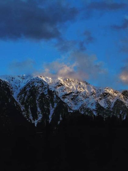 Another sunset moment in the mountains, where the last rays of light illuminate the snowy tops. The contrast with the dark foreground creates a sense of depth and tranquility.