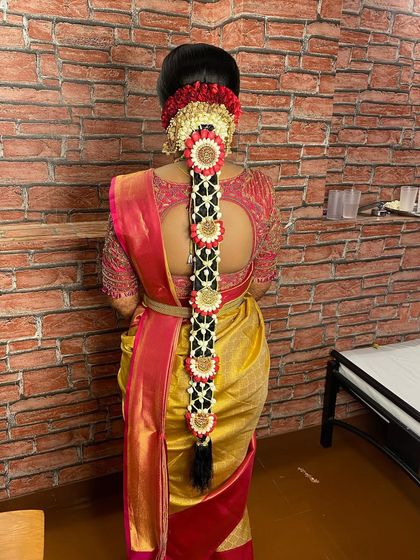 This traditional bridal braid is decorated with a net of flowers and custom floral jewellery pieces, perfectly matching the red and gold muhurtham saree.