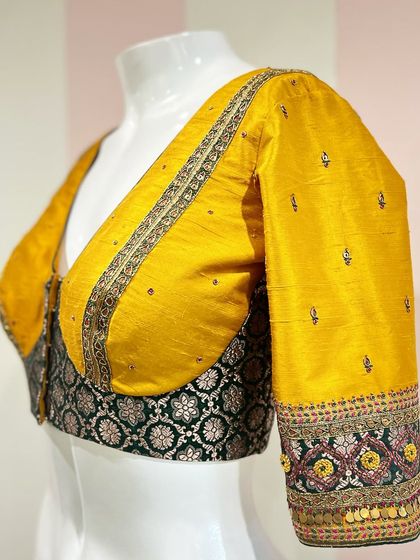 A statement saree blouse featuring a play of colors and embroidery techniques, with a deep V-neck and heavily embellished sleeves.