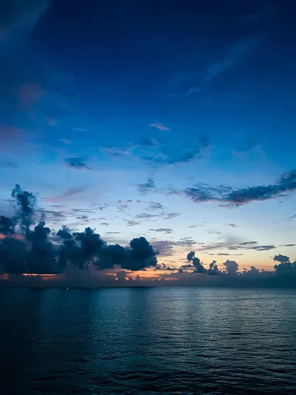 A breathtaking sunset over the open ocean, as seen from the deck of a cruise ship. The deep blues and subtle oranges create a serene and powerful seascape.