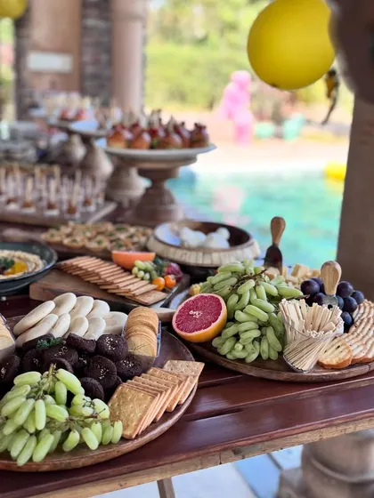 A beautiful poolside catering setup. The grazing tables feature an assortment of crackers, dips, cheeses, and fresh fruits, perfect for a relaxed yet elegant outdoor event.